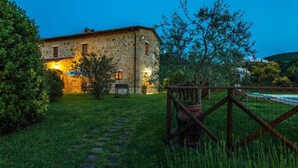 A stone building with a well-lit exterior, a grassy yard, and a pool area. - Si-g602-pien0at - Podere Bagnolo 8 (Pienza)
