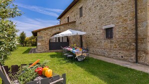 A stone building with a covered patio area, outdoor seating, and a grill with vegetables. - Si-g602-pien0at - Podere Bagnolo 8 (Pienza)