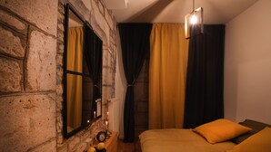 A room with a stone wall, a bed with yellow bedding, a nightstand with a lamp, and a mirror. - Apartment with sauna at the foot of the Citadel (Besançon)