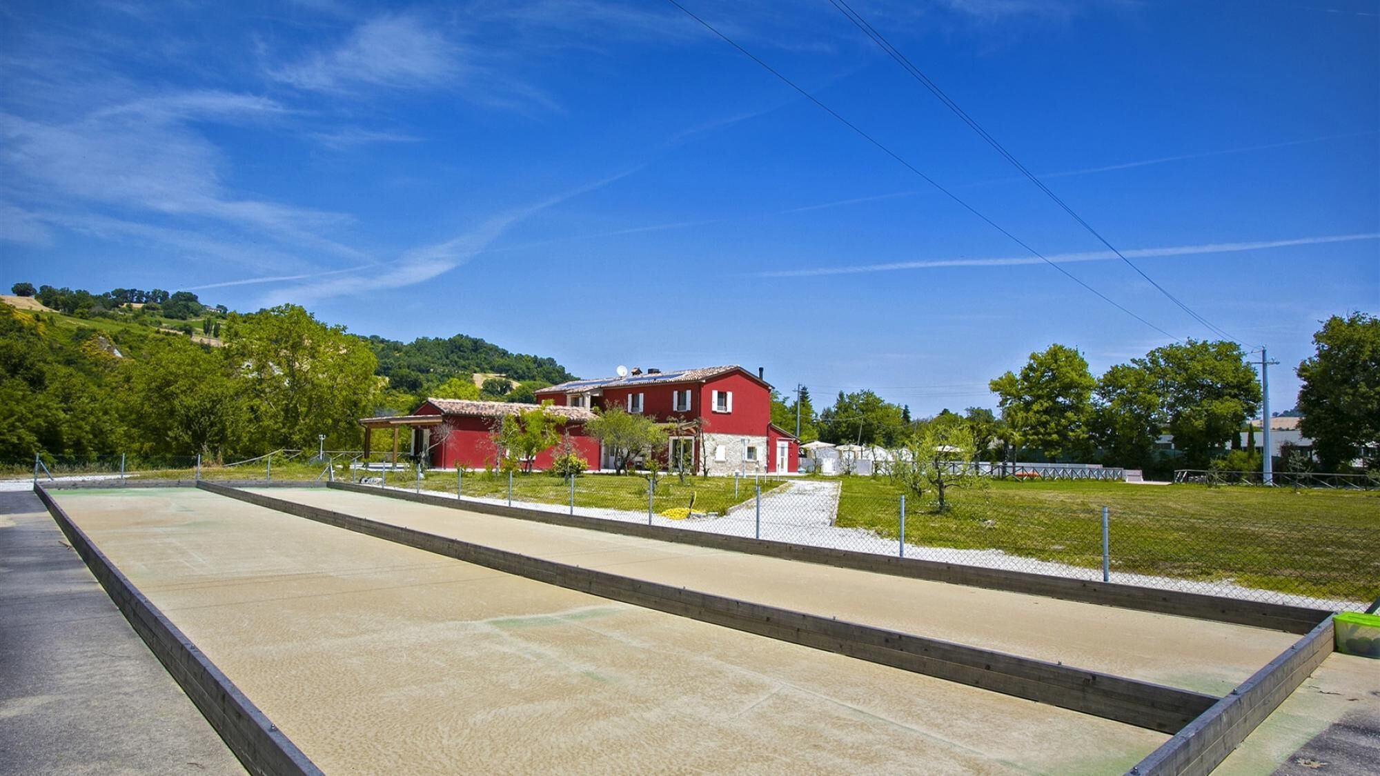 Ein rotes Gebäude mit flachem Dach, umgeben von einem eingezäunten Bereich mit einer Wiese und Bäumen.