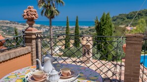 A table with a teapot, cups, and saucers on a colorful tablecloth, overlooking a scenic view of the sea and hills. - Ap-a047-cfpe10at - Fontespina 6 (Acquaviva Picena)