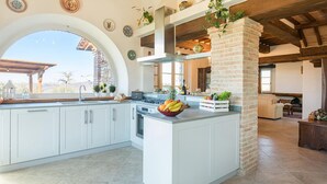 A spacious kitchen with a large island, white cabinetry, and a stone fireplace. - Pg-c744-cipi0at - La Villetta di Dante 6 (Citta della Pieve)