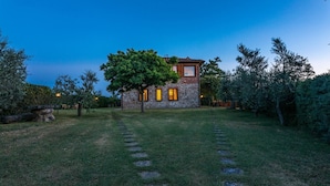 Une maison en pierre, avec un grand arbre devant, entourée d’une pelouse bien entretenue et de marches en pierre menant à l’entrée.