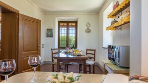 Un coin repas avec une table en bois dressée pour le repas, un verre à vin et une vue sur l’extérieur par une fenêtre.