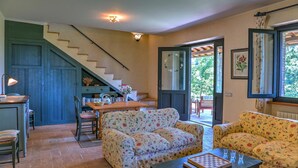 A cozy living room with a staircase, floral-patterned sofas, a wooden table, and a view through a glass door. - Tr-a691-basc0at - Villa Poggio Verde 6 (Baschi)