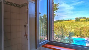 A bathroom with a shower, a window with a view of a vineyard and a pool. - Tr-a691-basc0at - Villa Poggio Verde 6 (Baschi)