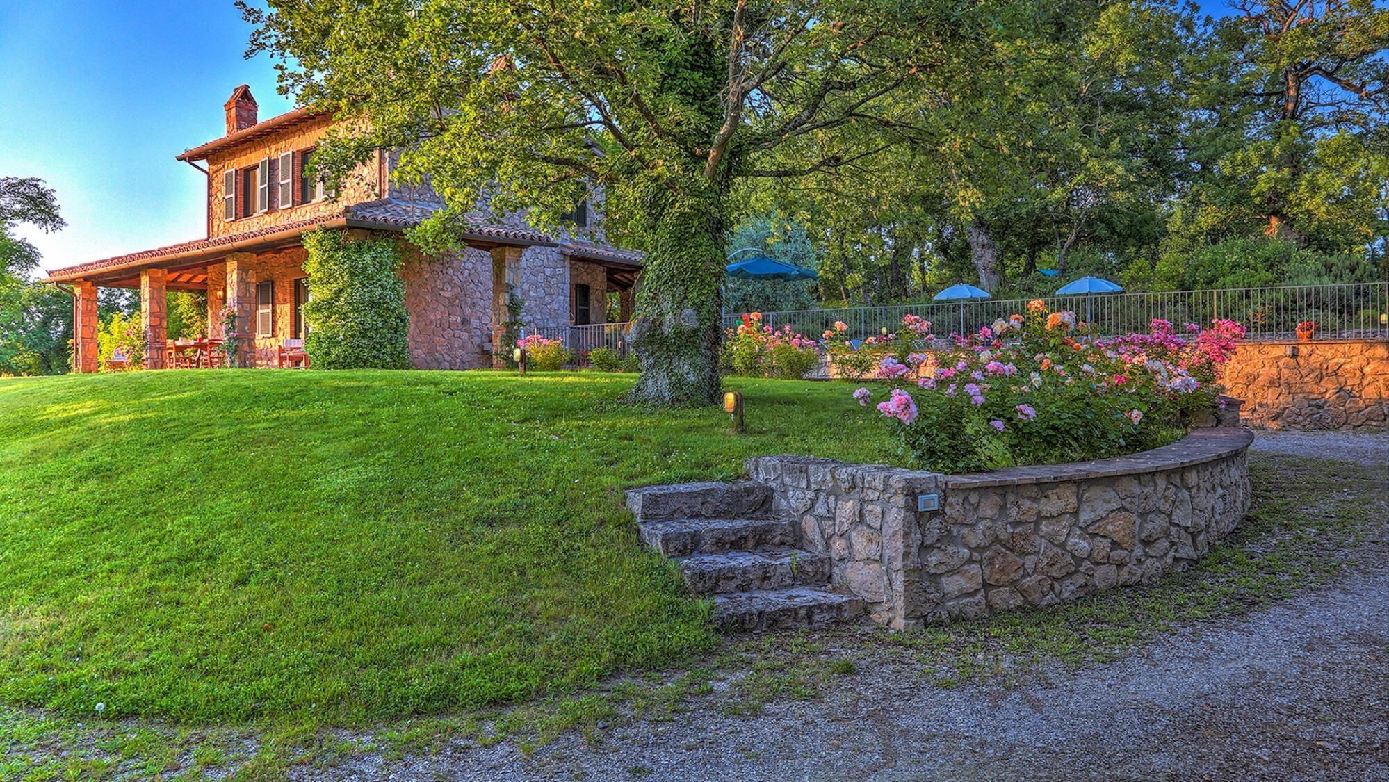 Une maison en pierre dotée d’un porche abrité, d’une pelouse parfaitement entretenue et d’un escalier en pierre menant à l’entrée.