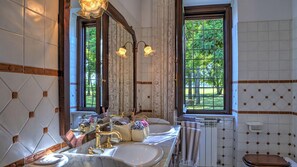 Ein Badezimmer mit zwei Waschbecken, einem großen Spiegel und einem Fenster mit Blick auf Grünflächen.