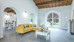 Un amplio salón con un sofá amarillo, una mesita de centro con fruta y un ventanal con vistas al jardín.