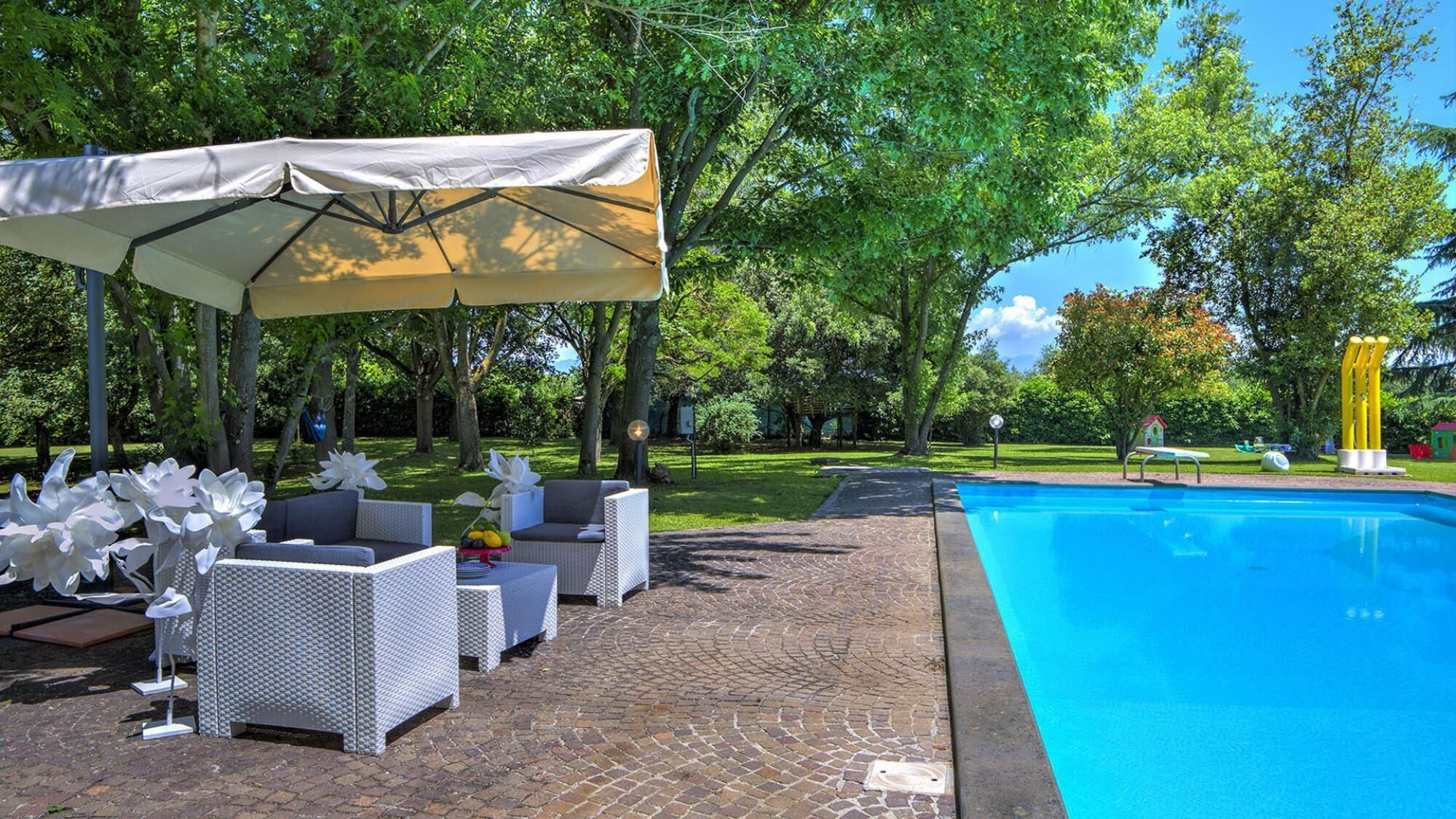 A poolside area with a covered seating area, a brick pathway, and a clear blue pool.