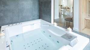 Un baño moderno con una bañera grande, un espejo y una zona de estar con una mesa y sillas.