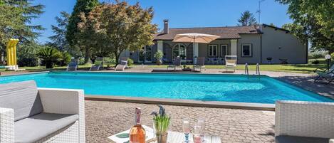 A poolside area with a clear view of a building, lounge chairs, and a table with drinks and fruit.