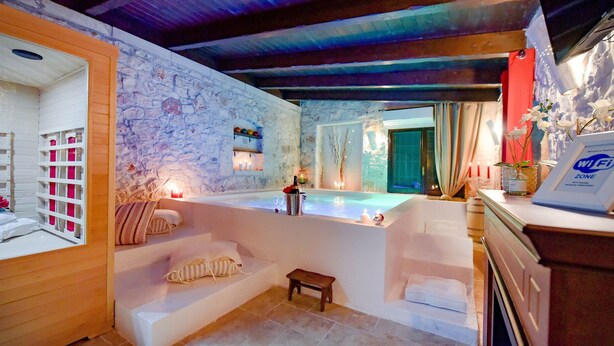 Ein Wellnessbereich mit einer Steinwand, einer Badewanne und einer kleinen Holzbank.