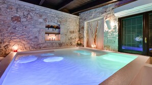 Ein Spa-Bereich mit Steinwänden, einem beheizten Pool, Kerzen und einem dekorativen Wandschrank.