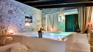 Ein Wellnessbereich mit Steinwand, einer großen Badewanne, Kerzen und einer Champagnerflasche.