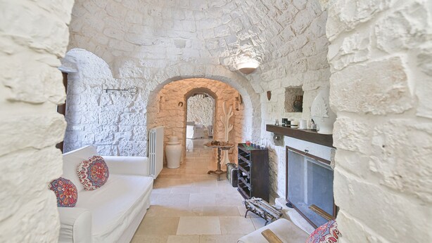 Quarto com paredes de pedra, um sofá branco, uma lareira e uma mesa de xadrez.