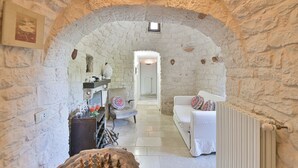 Interior com paredes de pedra, um sofá branco, uma mesa de madeira com copos e um tabuleiro de xadrez.