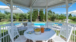 A covered outdoor seating area with a pool, white furniture, and a view of a staircase leading to a building. - Fm-l279-tspa0at - Il Podere di Fi 8 (Torre San Patrizio)