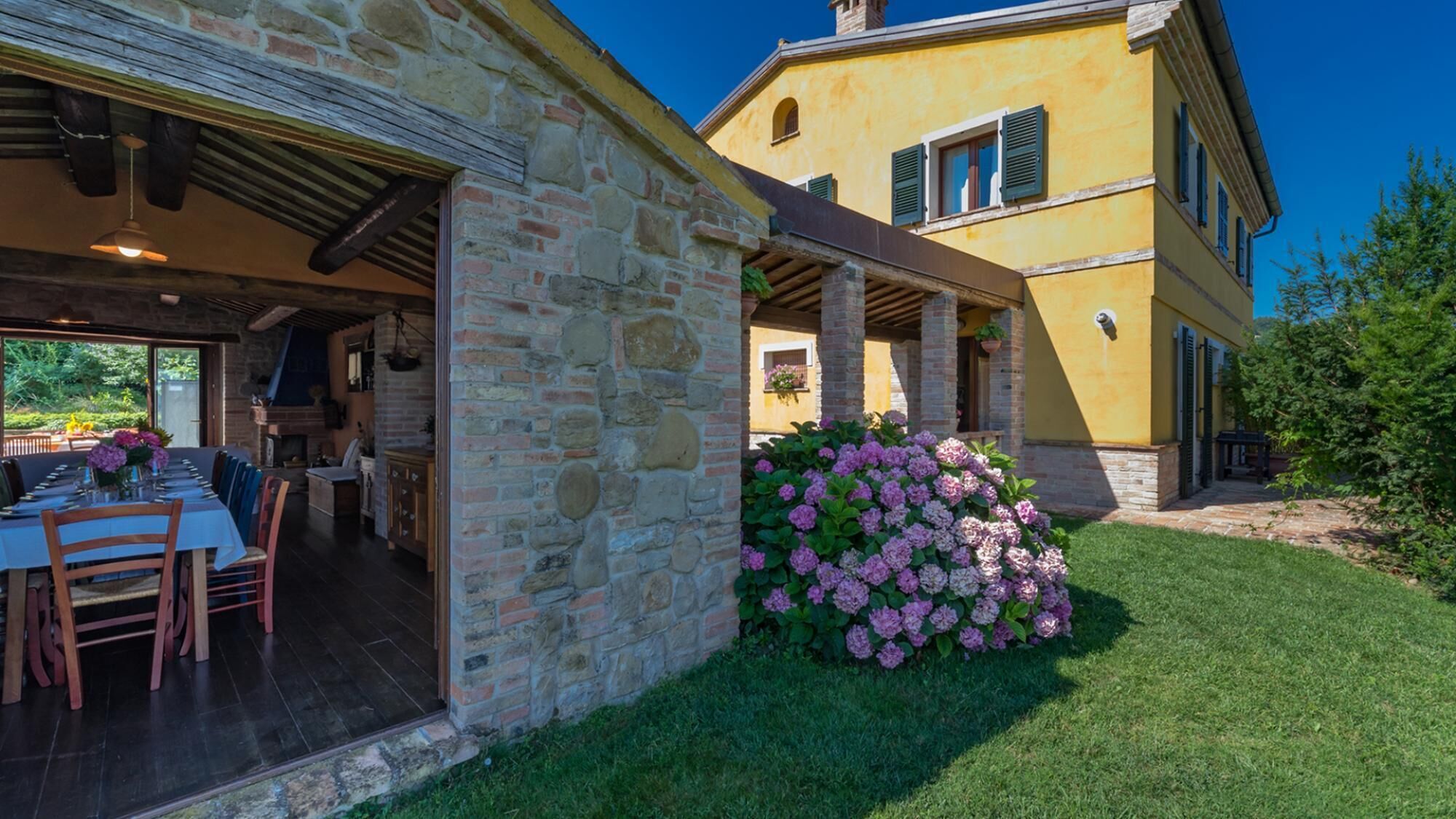 A stone building with a dining area and a garden with pink flowers.