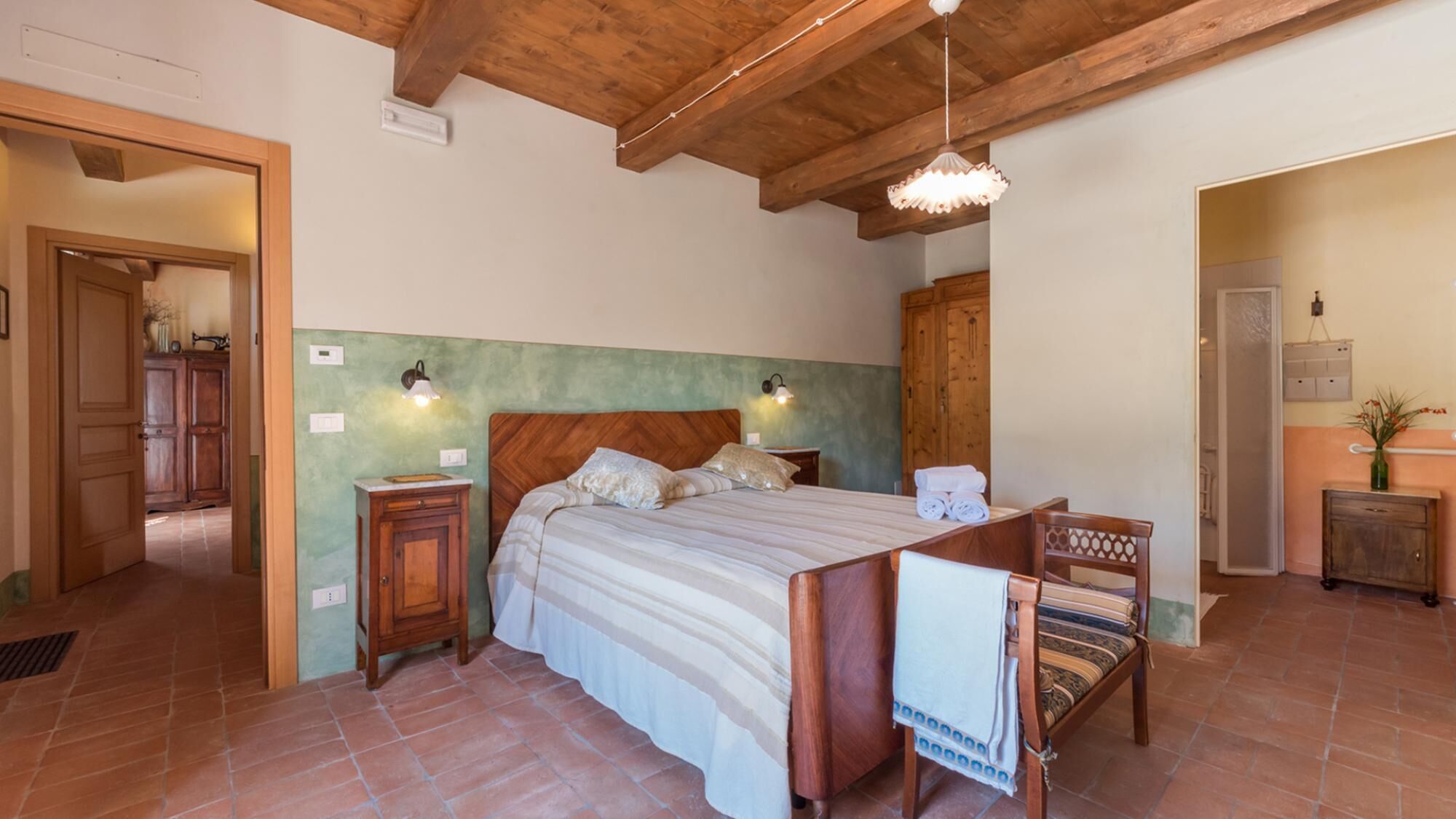 Un dormitorio con cama de madera, dos lámparas de noche, un armario de madera y un baño visible a través de una puerta abierta.