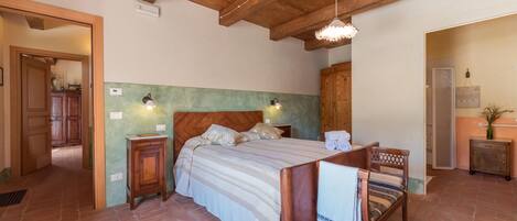 Un dormitorio con cama de madera, dos lámparas de noche, un armario de madera y un baño visible a través de una puerta abierta.