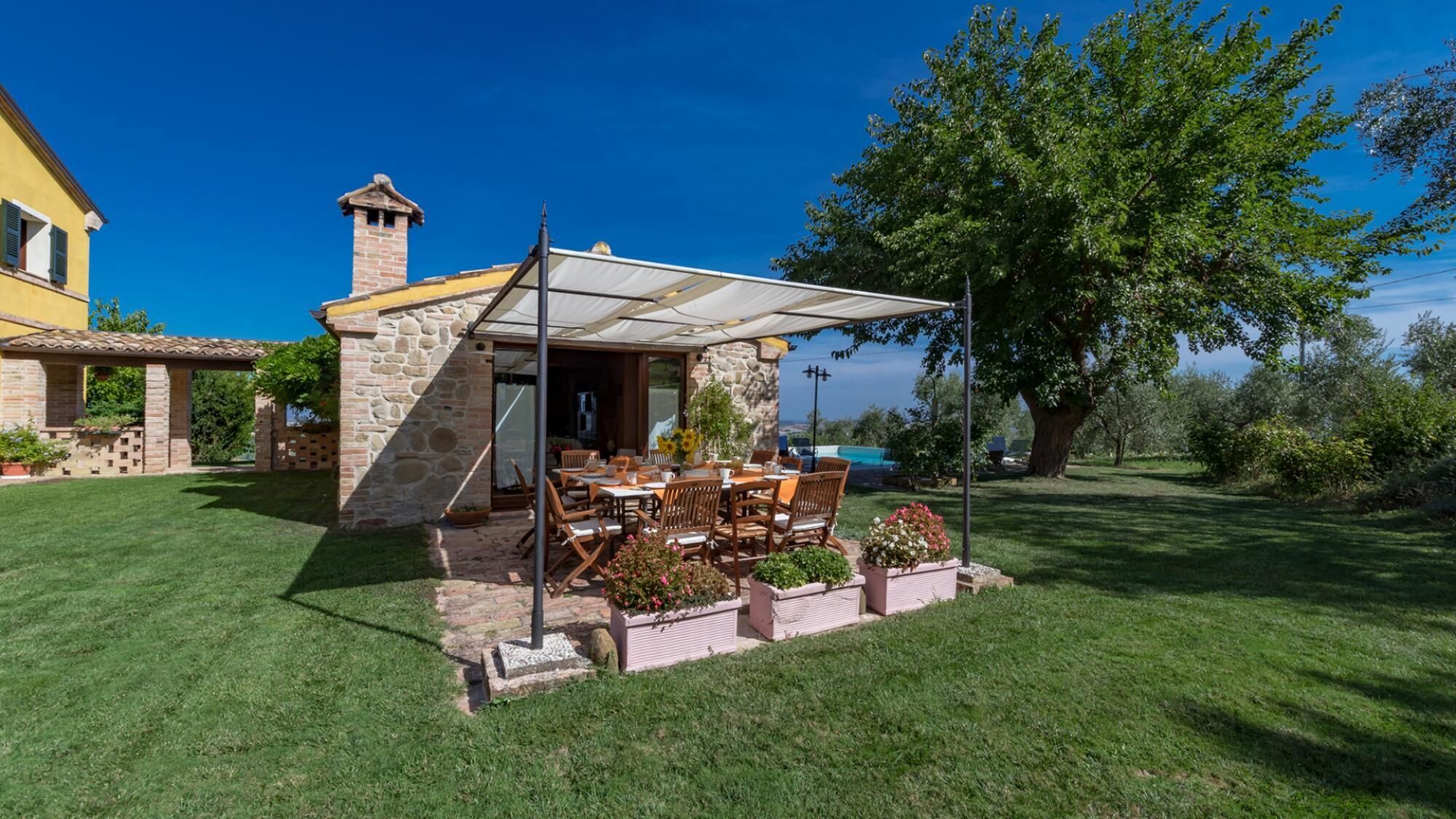 Un edificio de piedra con un patio cubierto, mesas al aire libre y vista al mar.