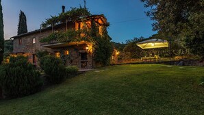 Uma casa de pedra com varanda, gramado bem cuidado e área de estar coberta ao ar livre.