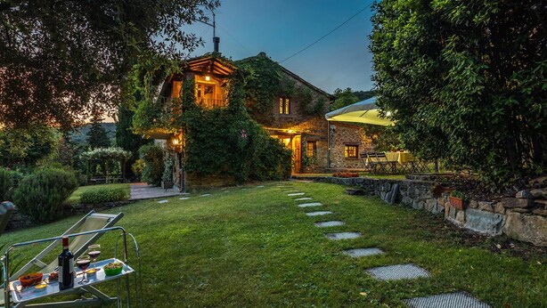 Uma casa de pedra com um gramado bem cuidado e uma área de refeições com mesas ao ar livre.