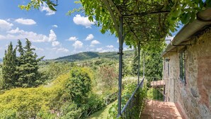 Edifício de pedra com varanda voltada para uma paisagem verdejante, com árvores e colinas.