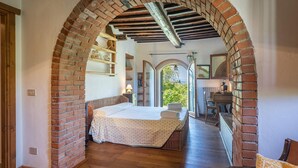 Quarto com cama, escrivaninha e cadeira, conectado por uma estrutura de tijolos em arco.
