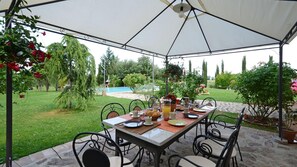 An outdoor patio with a table set for breakfast, surrounded by chairs, under a large umbrella.