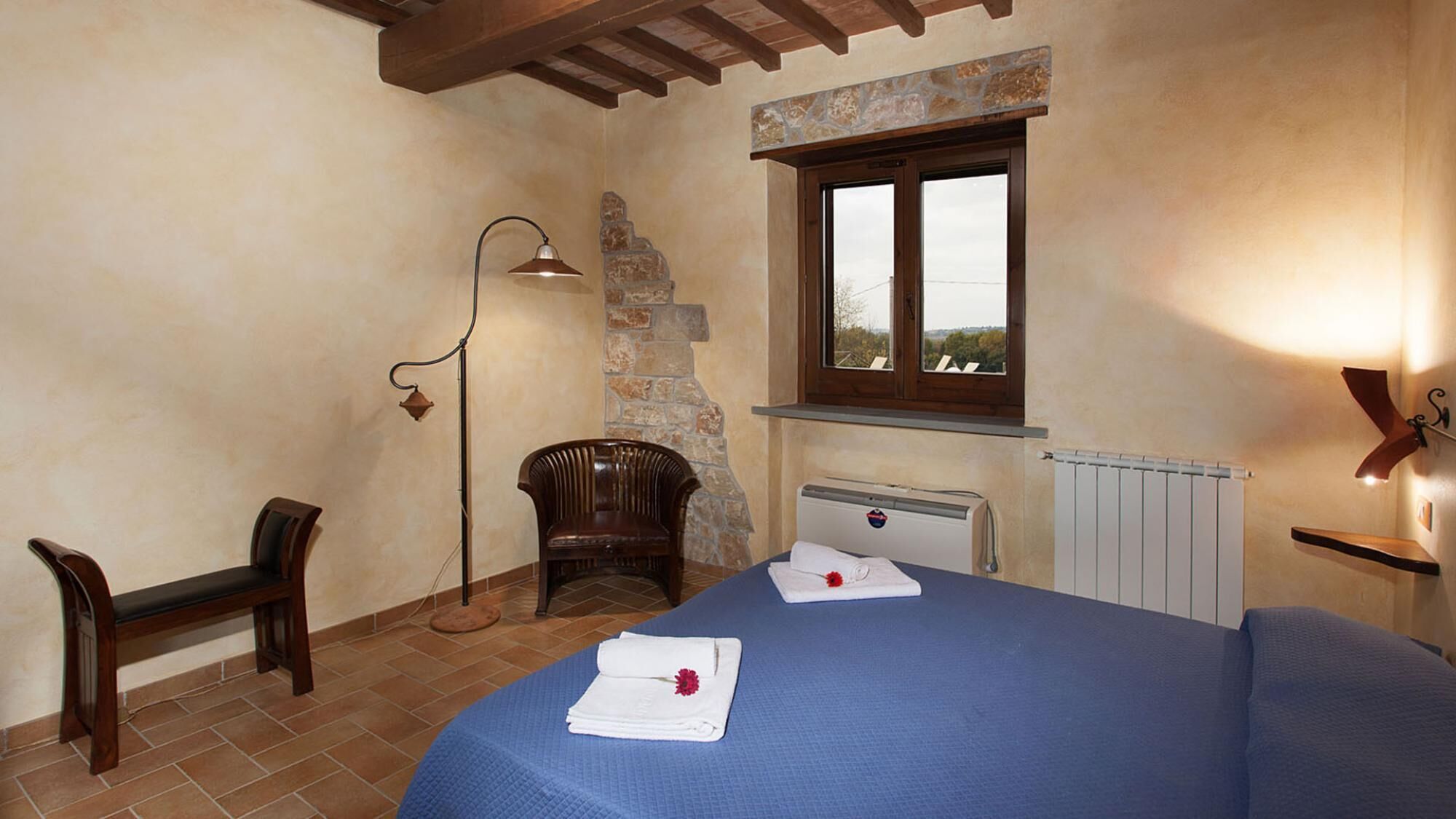 Une chambre à coucher comprenant un lit, une chaise, un bureau, une lampe, une fenêtre et un radiateur.
