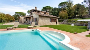 Une maison en pierre avec une piscine, deux chaises longues et une pelouse bien entretenue.