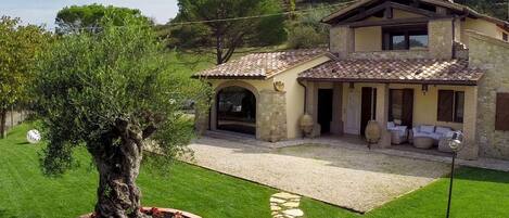 Une maison en pierre à deux étages, avec un toit en tuiles, un patio couvert et une pelouse bien entretenue.
