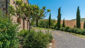 Un edificio in pietra con vialetto sterrato che conduce a un giardino rigoglioso, pieno di piante e alberi.