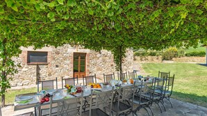 Un'area pranzo all'aperto con un edificio in pietra sullo sfondo, ricoperta da una vite.
