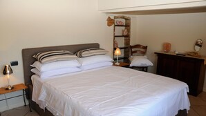 A neatly made bed with white linens and striped pillows, a bedside lamp, and a small wooden nightstand. - Bs-i633-viem71a1 - Arcimboldo House 2 2 (Sirmione)