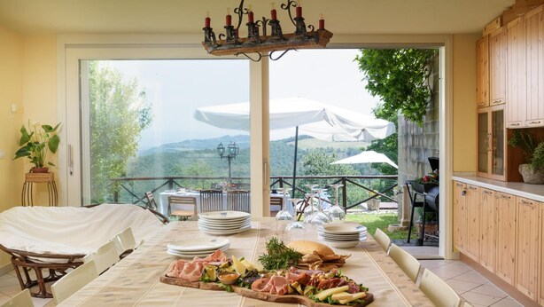 A dining area with a table set for a meal, a view of the outdoors, and a wooden cabinet. - Ar-a291-loto0at - Villa Vittoria d Anghiari 7 3 (Anghiari)