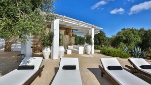 A sunlit outdoor lounge area with white lounge chairs, a stone wall, and potted plants. - Le-c336-sp2140bt - Villa Pajare Francesi 8 2 (Castrignano del Capo)