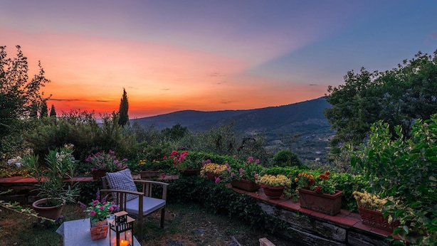 Un patio jardín con vistas a un atardecer sobre un paisaje montañoso.
