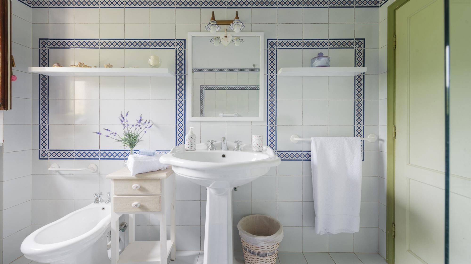 A bathroom with a toilet, bidet, sink, and shelves with toiletries.