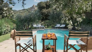 A poolside area with lounge chairs, a table with fruits and a drink, and a view of a hilltop building.