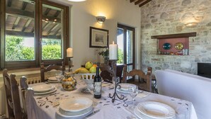A dining table set with plates, glasses, and a bottle of wine, surrounded by stone walls and wooden beams. - Tr-i381-vena0at - Casale al Doglio 6 1 (San Venanzo)