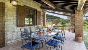 A covered outdoor dining area with a stone wall, wooden shutters, and a view of the countryside. - Tr-i381-vena0at - Casale al Doglio 6 1 (San Venanzo)