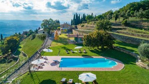 A large swimming pool with sun loungers and umbrellas, surrounded by a well-maintained lawn and stone walls. - Ar-a390-arez0bt - Torre Ginestre 12 (Arezzo)