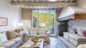 A cozy living room with two sofas, a coffee table with flowers, a stone wall, and a view of a green hillside. - Ar-a390-arez0bt - Torre Ginestre 12 (Arezzo)
