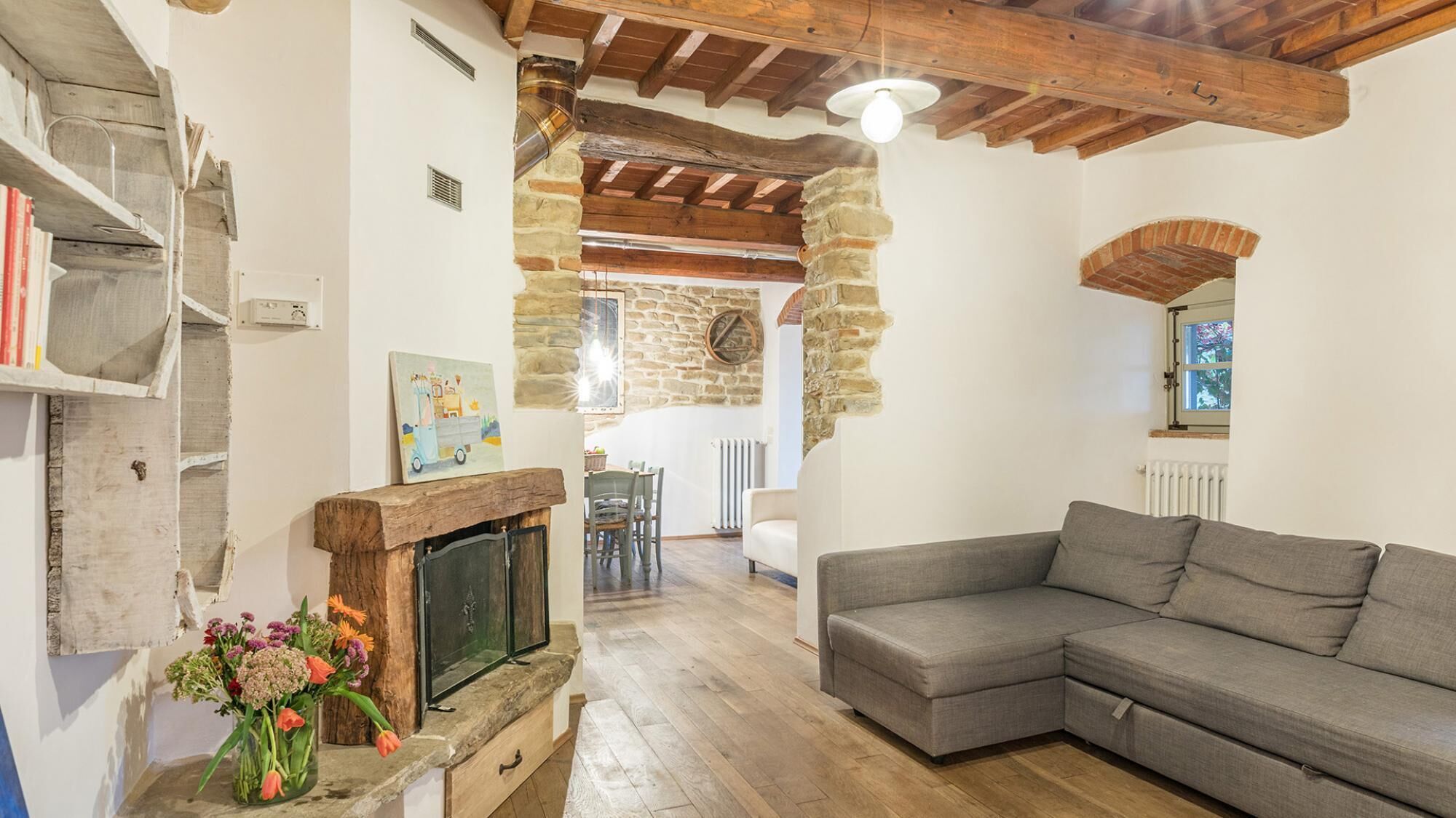 A cozy living room with a stone fireplace, a grey sofa, and a wooden ceiling.
