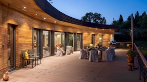 A modern outdoor dining area with a wooden deck and glass doors leading to an interior space.