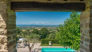 A stone archway framing a view of a swimming pool and a lush garden with a distant landscape. - Ar-d077-lper0at - La Torretta 10 (Cortona)