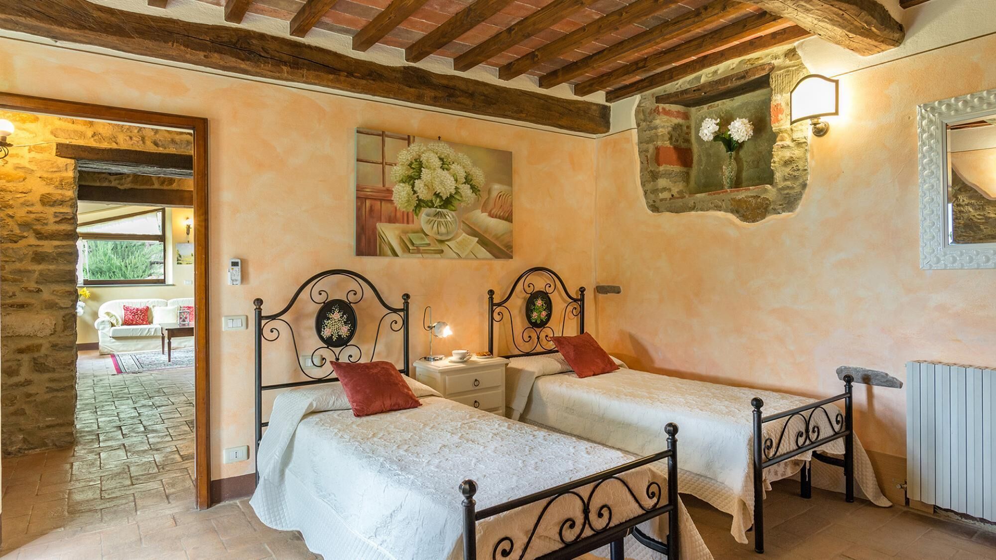 A bedroom with two beds, a stone wall, a wooden ceiling, and a small window with flowers.
